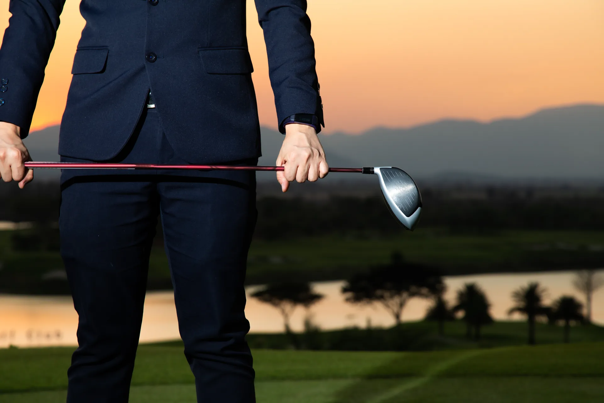 A businessman in a suit holding a golf driver at sunset